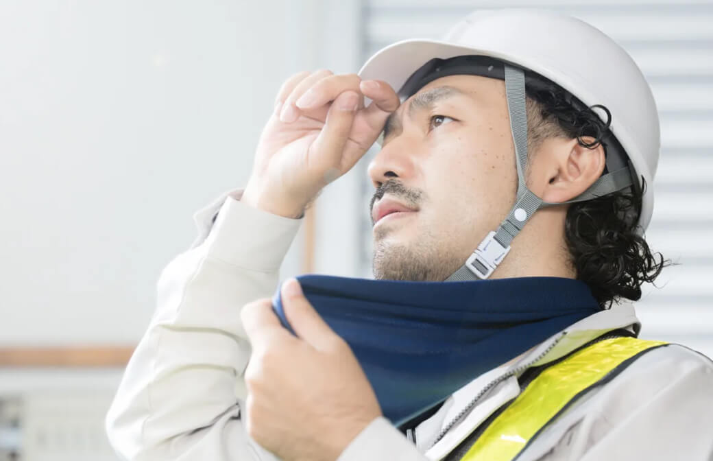 ヘルメットをかぶり、首にタオルを巻いた作業員の男性が汗を拭っている